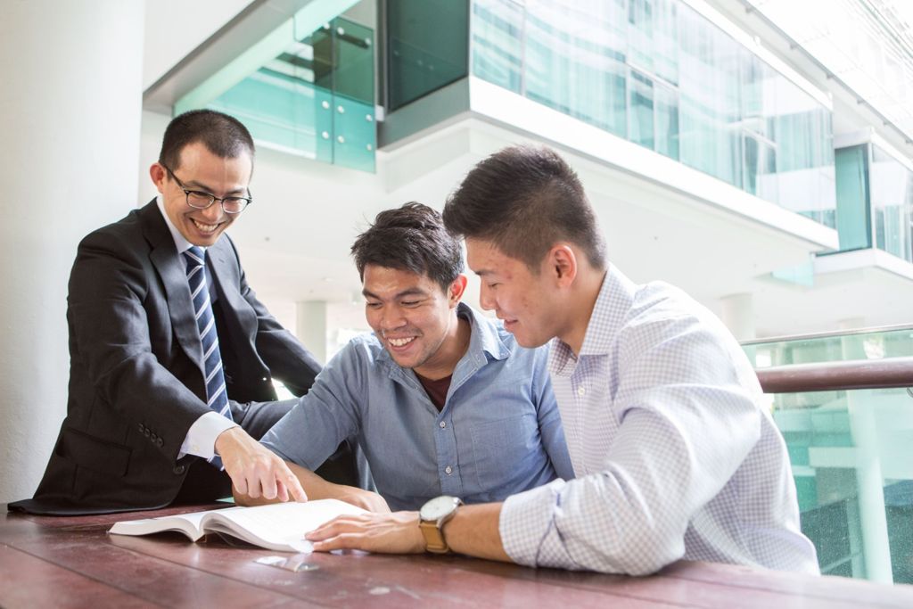 Miniature of Professor Hiro Saito having a discussion with two students in a brightly lit bench outside a classroom